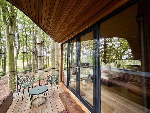 Balkon Moderne Terrasse mit Glasfront und Waldblick, ausgestattet mit Tisch, Stühlen und Holzdach.