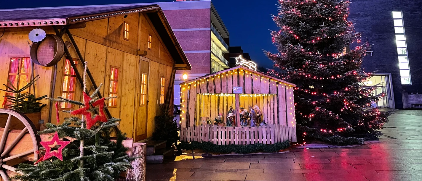 WM 1.JPG Beleuchtete Weihnachtsmarkthütte mit Krippe und großem Tannenbaum bei Nacht.