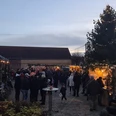 Löbnitzer Weihnachtsmarkt Das Bild zeigt einen Weihnachtsmarkt in der Dämmerung, mit Menschen, die sich um festlich geschmückte Stände und einen großen, beleuchteten Weihnachtsbaum versammeln, während die Lichter und Dekorationen eine gemütliche Atmosphäre schaffen.