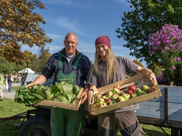 Obstwiesenfest Zwei Männer präsentieren stolz frisches Gemüse und Äpfel bei sonnigem Wetter auf einem Bauernmarkt.