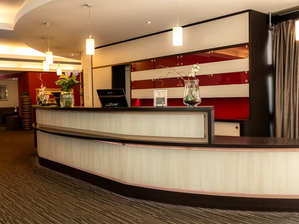 Rezeption.jpg Rezeption einer modernen Hotellobby mit geschwungener Theke, stilvoller Beleuchtung und Dekoration.