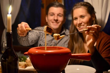 Twee personen genieten van een gezellige fondue met stukjes brood, romantisch bij kaarslicht.