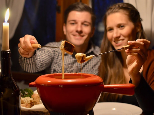 Two people enjoy a convivial fondue with pieces of bread, romantically by candlelight.