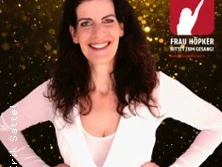 Porträt von Frau Höpker, lächelnd, in einem weißen Oberteil vor einem funkelnden Hintergrund.