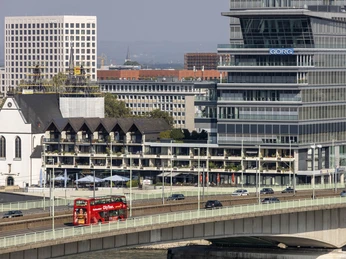 Cologne CityTour Ein roter Doppeldeckerbus der CityTour fährt auf einer Brücke an modernen Bürogebäuden vorbei.A red double-decker CityTour bus drives past modern office buildings on a bridge.