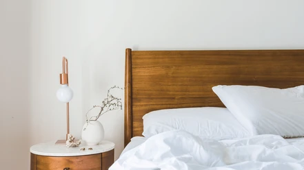 Hotel Stickdorn Destination One.png Ein einfach eingerichtetes Hotelzimmer mit einem hölzernen Bettgestell, weißen Kissen und Bettwäsche.