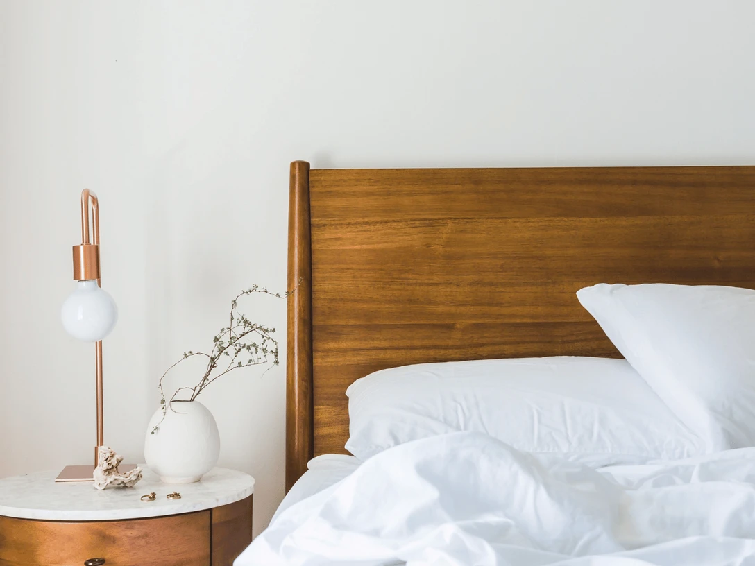 Hotel Stickdorn Destination One.png Ein einfach eingerichtetes Hotelzimmer mit einem hölzernen Bettgestell, weißen Kissen und Bettwäsche.