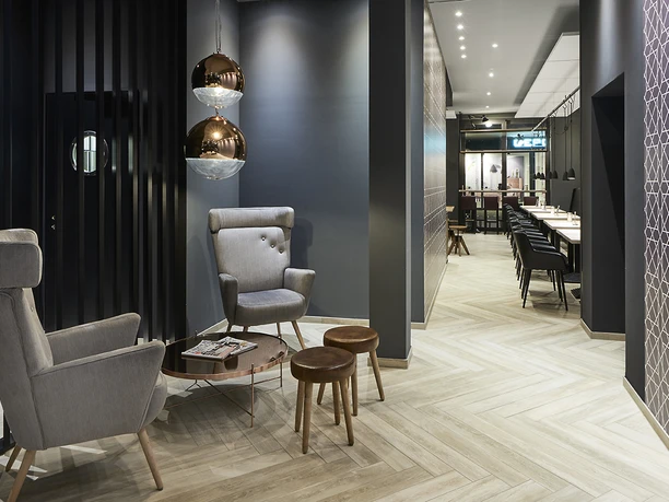 Moderner Frühstücksbereich mit stilvollen grauen Stühlen, kupfernen Hängeleuchten und langen Tischen.