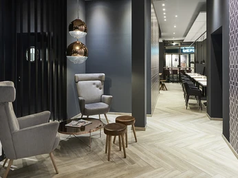 Herford-Hotel Hansa Frühstücksbereich © Hotel Hansa.jpg Moderner Frühstücksbereich mit stilvollen grauen Stühlen, kupfernen Hängeleuchten und langen Tischen.