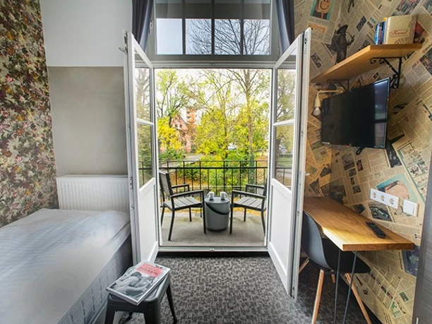 Ein modernes Hotelzimmer mit Balkonblick auf grüne Baumkronen und komfortabler Ausstattung.