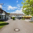 Herford-Hotel Waldesrand.jpg Hotelgebäude mit gepflastertem Vorplatz, dazwischen grüner Rasen und Bäume bei strahlend blauem Himmel.