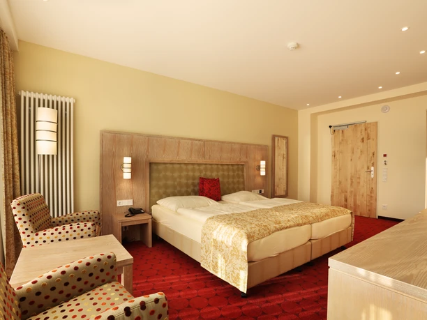 Hotel Waldesrand Herford.jpg Ein helles und einladendes Hotelzimmer mit zwei Sesseln, einem großen Bett und einem Schreibtisch.