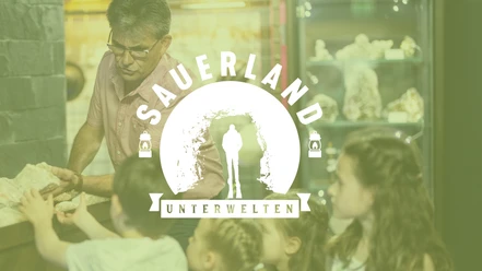 ST_Platzhalter für Führungen Erwachsener zeigt Kindern Gesteine in einer Ausstellung, darüber ein Logo