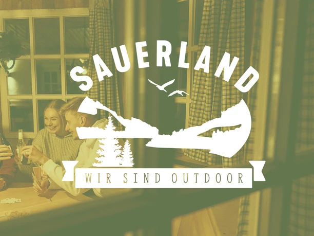 Drei Personen stoßen an einem Holztisch in einer Hütte miteinander an.