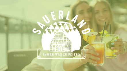 Zwei Personen stoßen mit bunten Cocktails an, während ein Sauerland‑Logo groß darüber liegt.