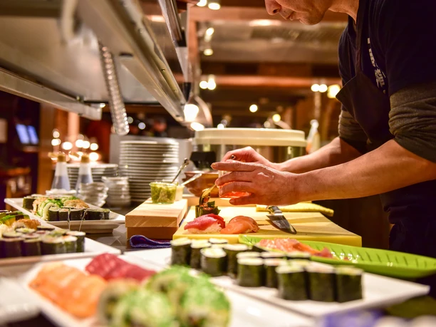 Küche Land Gut Höhne Ein Koch bereitet Sushispezialitäten auf einer offenen Theke in einem gehobenen Restaurant vor.