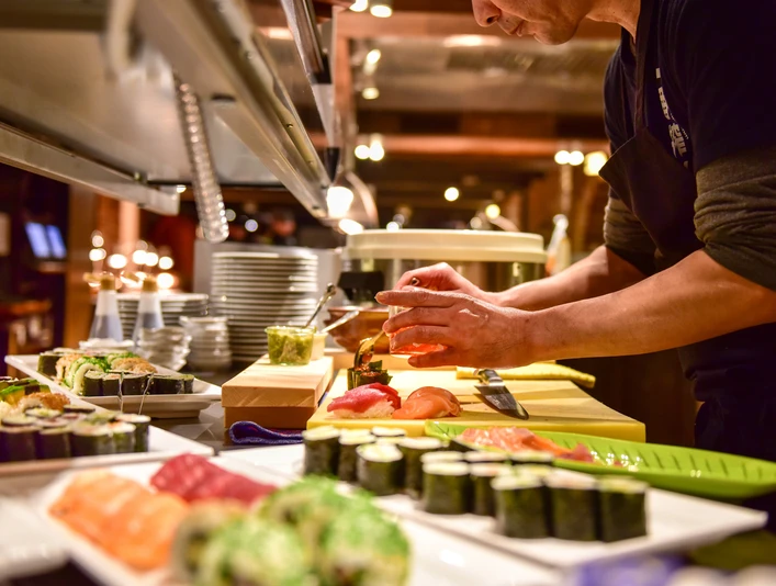 Küche Land Gut Höhne Ein Koch bereitet Sushispezialitäten auf einer offenen Theke in einem gehobenen Restaurant vor.