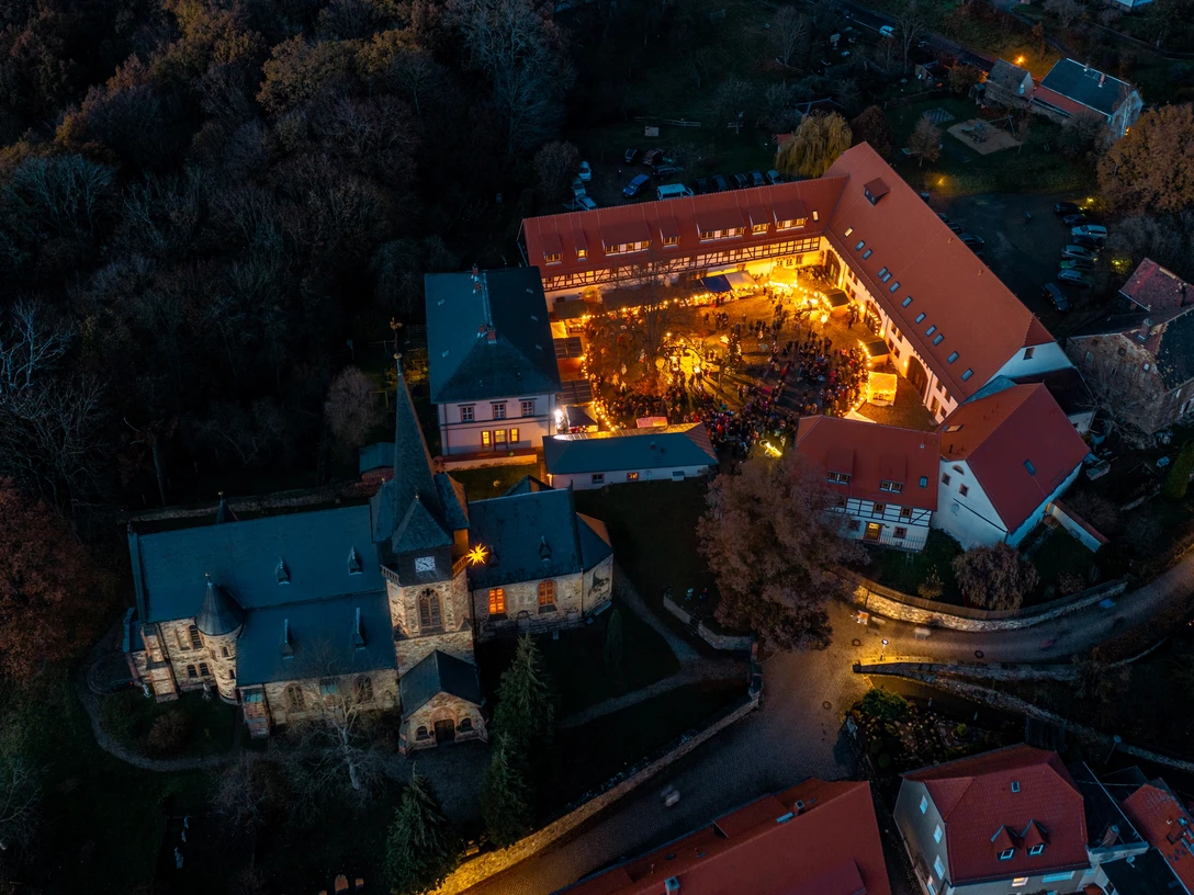 Weihnachtsmarkt Kohren-Sahlis Das Bild zeigt eine Luftaufnahme eines beleuchteten, historischen Gebäudekomplexes in herbstlicher Umgebung, in dem eine Veranstaltung mit zahlreichen Besuchern im Innenhof stattfindet.