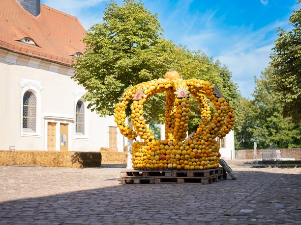 Kroneninstallation aus Kürbissen auf einem Schlossplatz unter blauem Himmel.