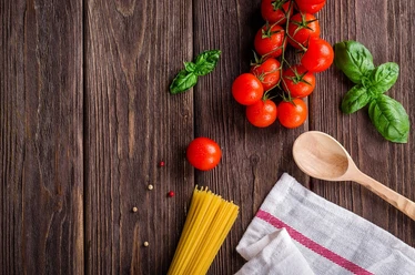 Spaghetti Tomaten, Basilikum, Spaghetti und ein Holzlöffel auf Holztisch.