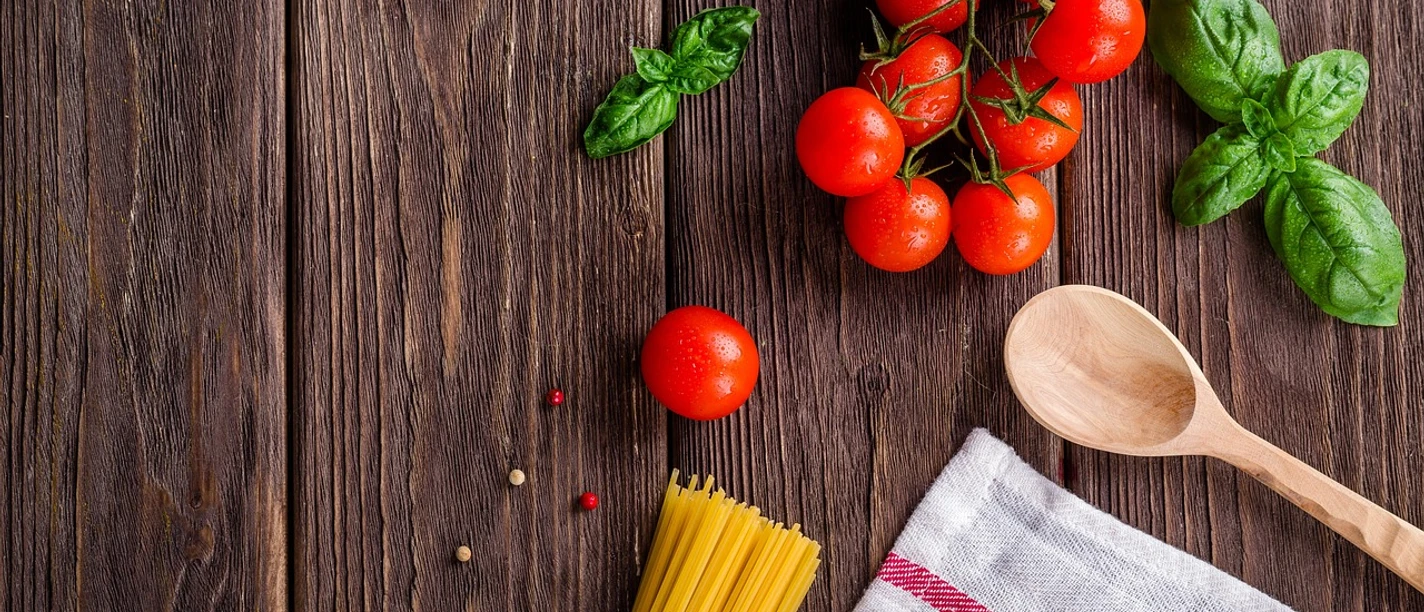 Spaghetti Tomaten, Basilikum, Spaghetti und ein Holzlöffel auf Holztisch.