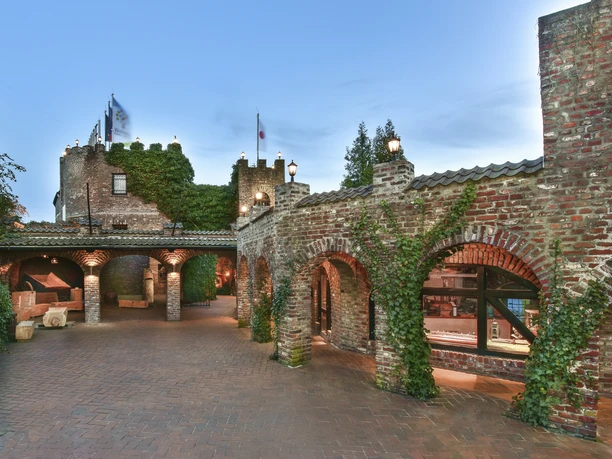 Land Gut Höhne Außenansicht des Eingangsbereiches Backsteingebäude mit begrünten Bögen und Fahnen, beleuchtet bei Dämmerung, im Eingangsbereich von Land Gut Höhne.