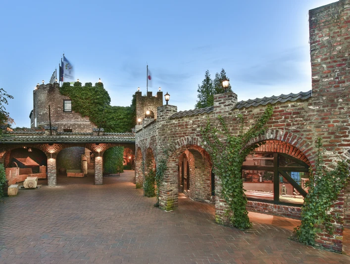 Land Gut Höhne Außenansicht des Eingangsbereiches Backsteingebäude mit begrünten Bögen und Fahnen, beleuchtet bei Dämmerung, im Eingangsbereich von Land Gut Höhne.