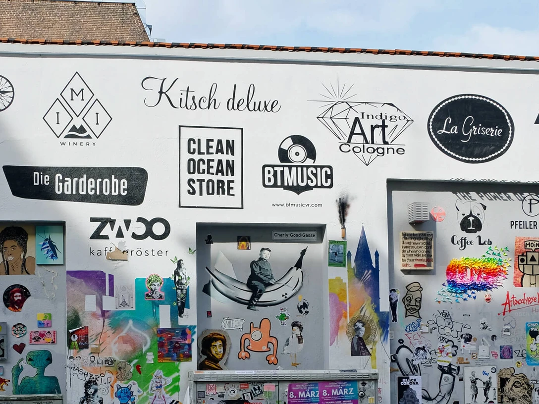 Körnerfeld Auf dem Bild ist ein Abschnitt einer kreativ gestalteten Wand in urbanem Umfeld zu sehen. Die Wand ist mit einer Vielzahl von bunten Postern, Schildern und Graffiti bedeckt. Einige der Logos und Schilder bewerben lokale Geschäfte.The picture shows a section of a creatively designed wall in an urban environment. The wall is covered with a variety of colorful posters, signs and graffiti. Some of the logos and signs advertise local businesses.