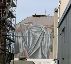 Mural Fassadenbild zeigt zwei Hände, die ein großes, graues Tuch in der Kölner Maybachstraße spannen.