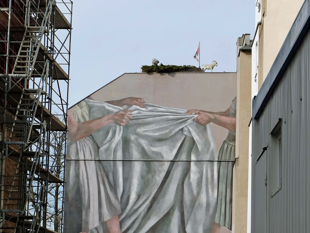 Mural Fassadenbild zeigt zwei Hände, die ein großes, graues Tuch in der Kölner Maybachstraße spannen.Facade picture shows two hands stretching a large, gray cloth in Cologne's Maybachstrasse.