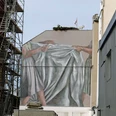 Mural Fassadenbild zeigt zwei Hände, die ein großes, graues Tuch in der Kölner Maybachstraße spannen.Facade picture shows two hands stretching a large, gray cloth in Cologne's Maybachstrasse.