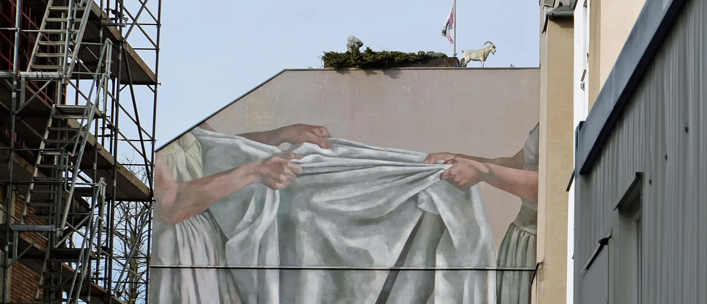 Mural Facade picture shows two hands stretching a large, gray cloth in Cologne's Maybachstrasse.