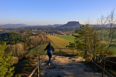 Rocky cliffs and coniferous forests with a view of a flat mountain silhouette in the background.