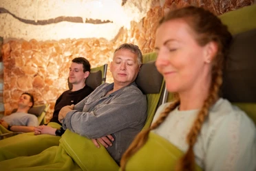Salzgrotte im Landhotel Annelie Vier Personen entspannen auf Liegestühlen, umgeben von Salzsteinwänden in einer beruhigenden Atmosphäre.