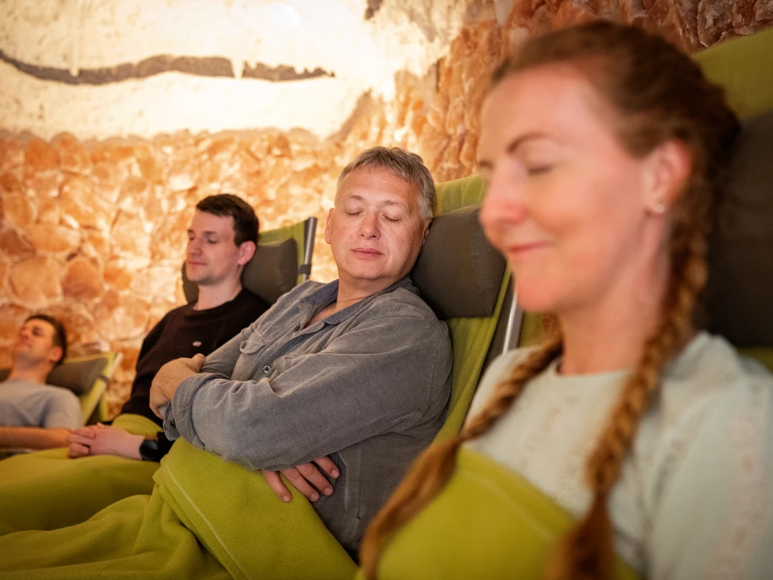 Salzgrotte im Landhotel Annelie Vier Personen entspannen auf Liegestühlen, umgeben von Salzsteinwänden in einer beruhigenden Atmosphäre.