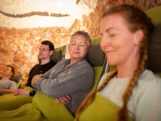 Salzgrotte im Landhotel Annelie Vier Personen entspannen auf Liegestühlen, umgeben von Salzsteinwänden in einer beruhigenden Atmosphäre.