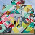 Mural Buntes geometrisches Wandbild an einem Hochhaus mit leuchtenden Farben und abstrakten Formen.Colorful geometric mural on a high-rise building with bright colors and abstract shapes.