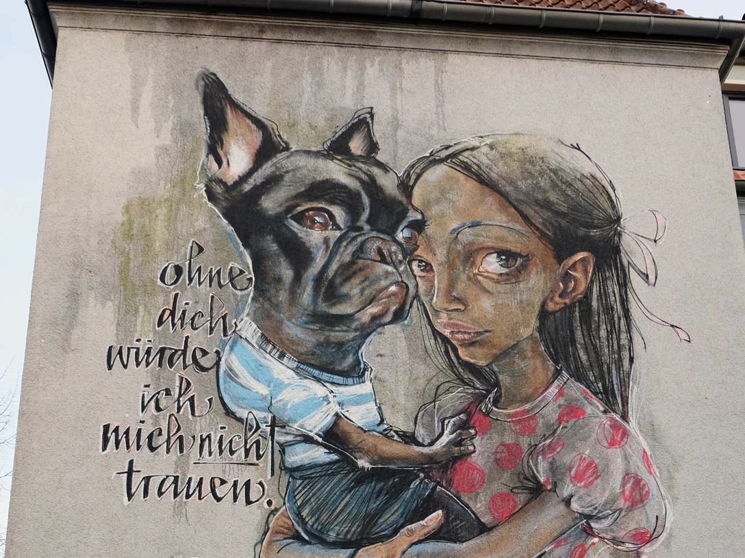 Mural Ein Mural zeigt ein Mädchen, das einen Hund liebevoll umarmt. Daneben steht der Text: „ohne dich würde ich mich nicht trauen.“One mural shows a girl lovingly hugging a dog. Next to it is the text: "Without you, I wouldn't dare."