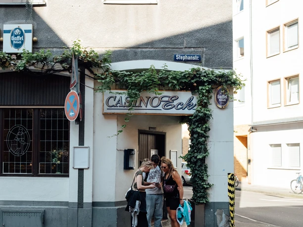 Mindwalk in Köln Eine Gruppe von Menschen steht vor einem historischen Kölner Eckgeschäft mit Schildern von Gaffel Kölsch.