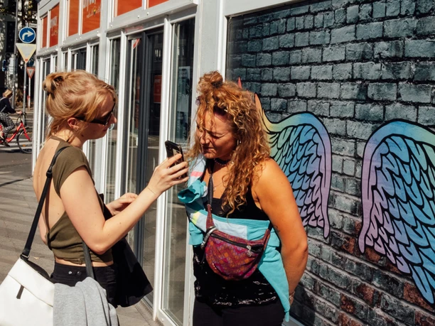 Mindwalk in Köln Zwei Menschen posieren vor einer farbenfrohen Wand mit bunten Flügeln, die sie spielerisch darstellen.