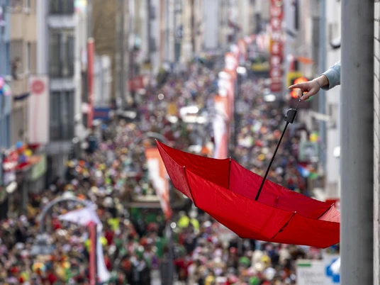 Rosenmontagszug Roter Schirm, aufgespannt über einer Menschenmenge beim Kölner Rosenmontagszug.Red umbrella stretched over a crowd at the Cologne Rose Monday parade.Een rode paraplu overspant een menigte tijdens de parade op Roze Maandag in Keulen.