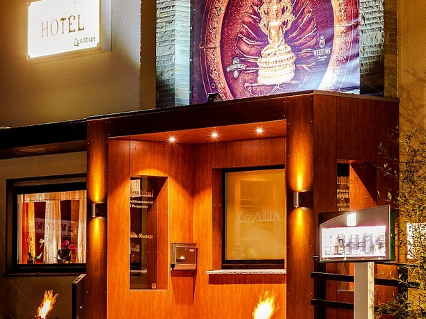 Eingang eines thailändischen Restaurants mit warmer Holzfassade und beleuchtetem Werbeschild.