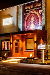 RoyalThai (12).jpg Eingang eines thailändischen Restaurants mit warmer Holzfassade und beleuchtetem Werbeschild.