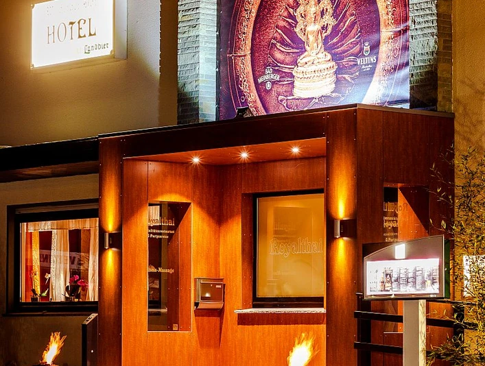 RoyalThai (12).jpg Eingang eines thailändischen Restaurants mit warmer Holzfassade und beleuchtetem Werbeschild.