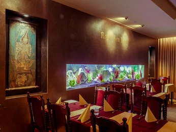 RoyalThai (10).jpg In einem elegant dekorierten Restaurant an einer dunklen Wand glänzt ein beleuchtetes, buntes Aquarium.