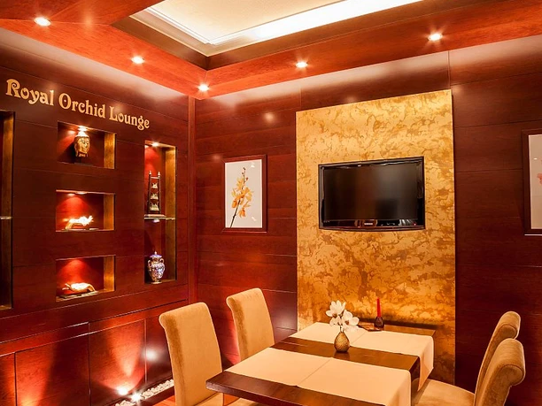 Eleganter Raum mit Holzwänden, quadratischem Tisch, vier beigen Stühlen und dezenter Beleuchtung.