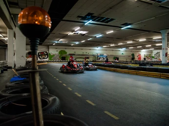 Zwei Personen fahren Gokarts auf einer Indoor-Kartbahn mit Kurven und Reifenbegrenzungen.