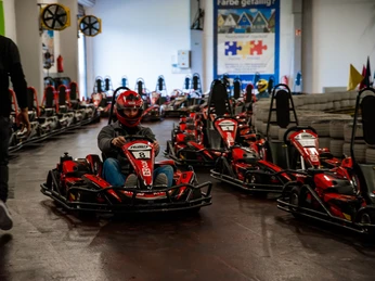 Eine Indoor-Kartbahn mit mehreren roten Karts. Ein Fahrer trägt Helm und Schutzkleidung.
