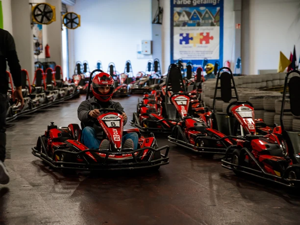Eine Indoor-Kartbahn mit mehreren roten Karts. Ein Fahrer trägt Helm und Schutzkleidung.