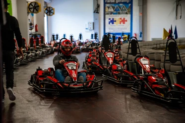 Eine Indoor-Kartbahn mit mehreren roten Karts. Ein Fahrer trägt Helm und Schutzkleidung.